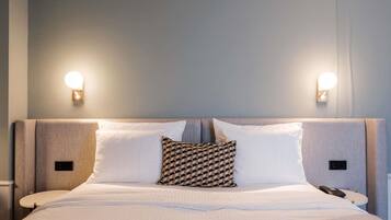 A neatly made bed with white linens, a patterned pillow, and two bedside tables with lamps.