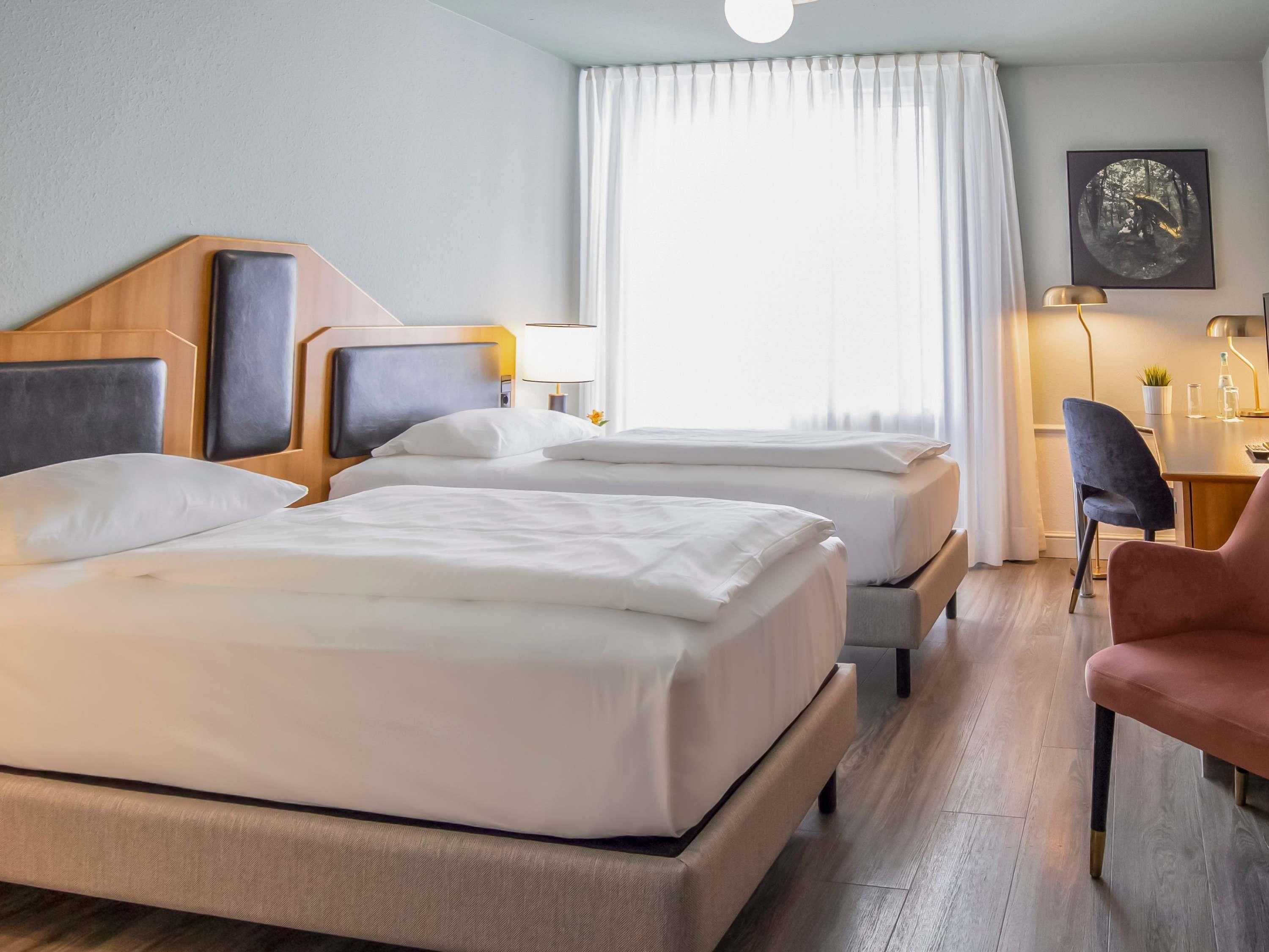 A hotel room with two beds, a desk, a chair, and a painting on the wall.