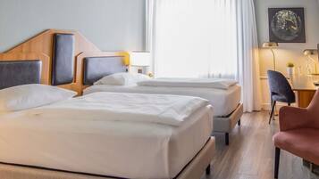 A hotel room with two beds, a desk, a chair, and a painting on the wall.