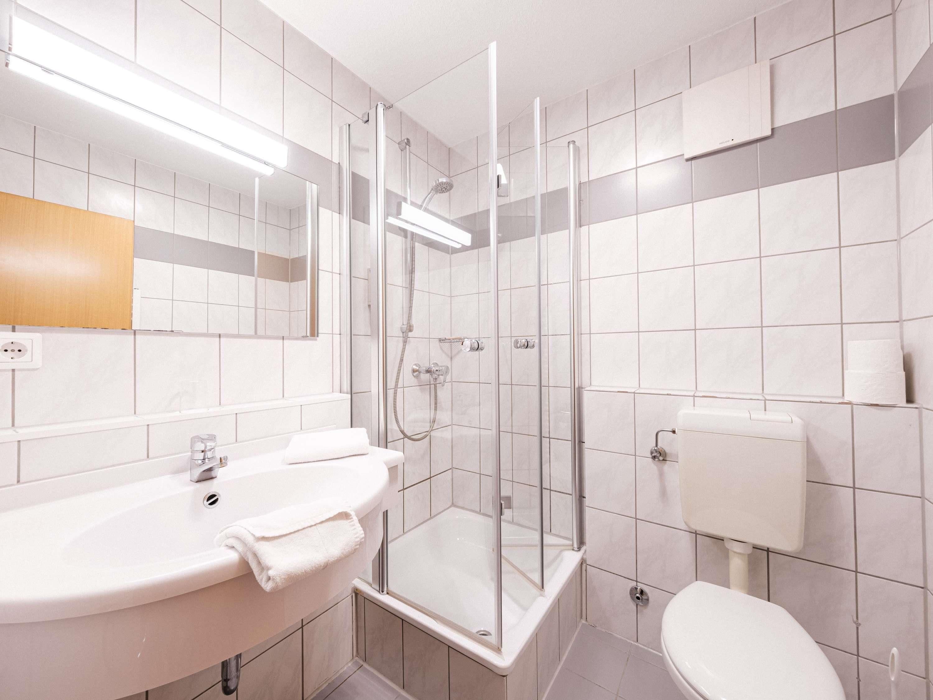 Un baño moderno con ducha acristalada, lavamanos con toalla e inodoro.