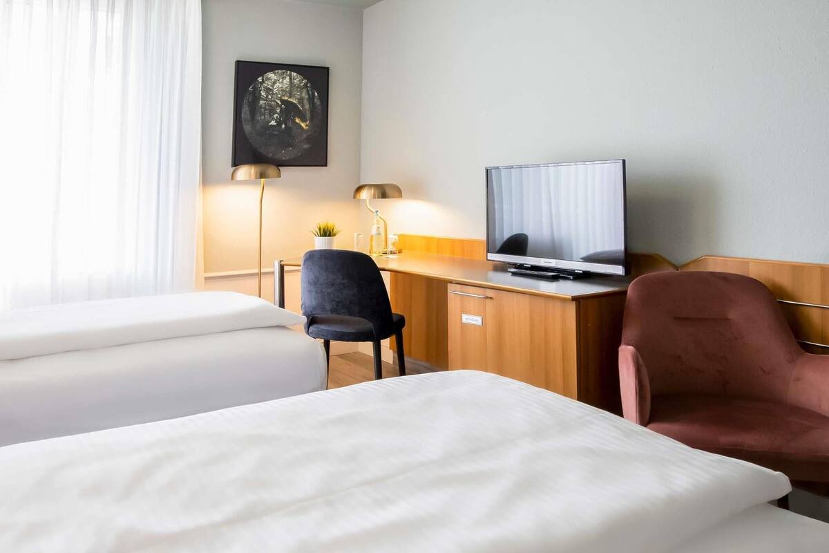A hotel room with two beds, a desk with a television, a chair, and a wall-mounted picture.