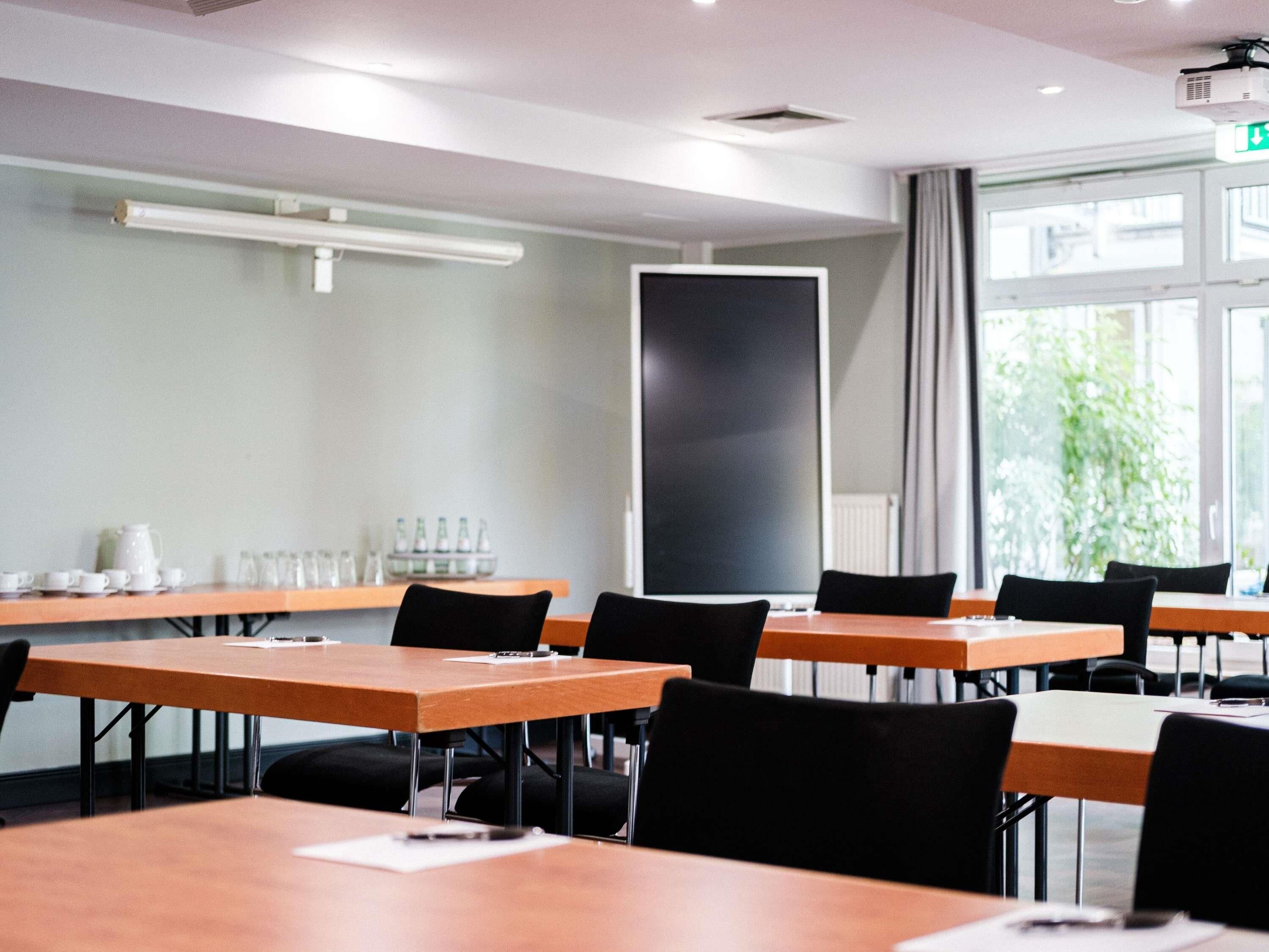 A conference room with tables, chairs, a projector, and a large window.