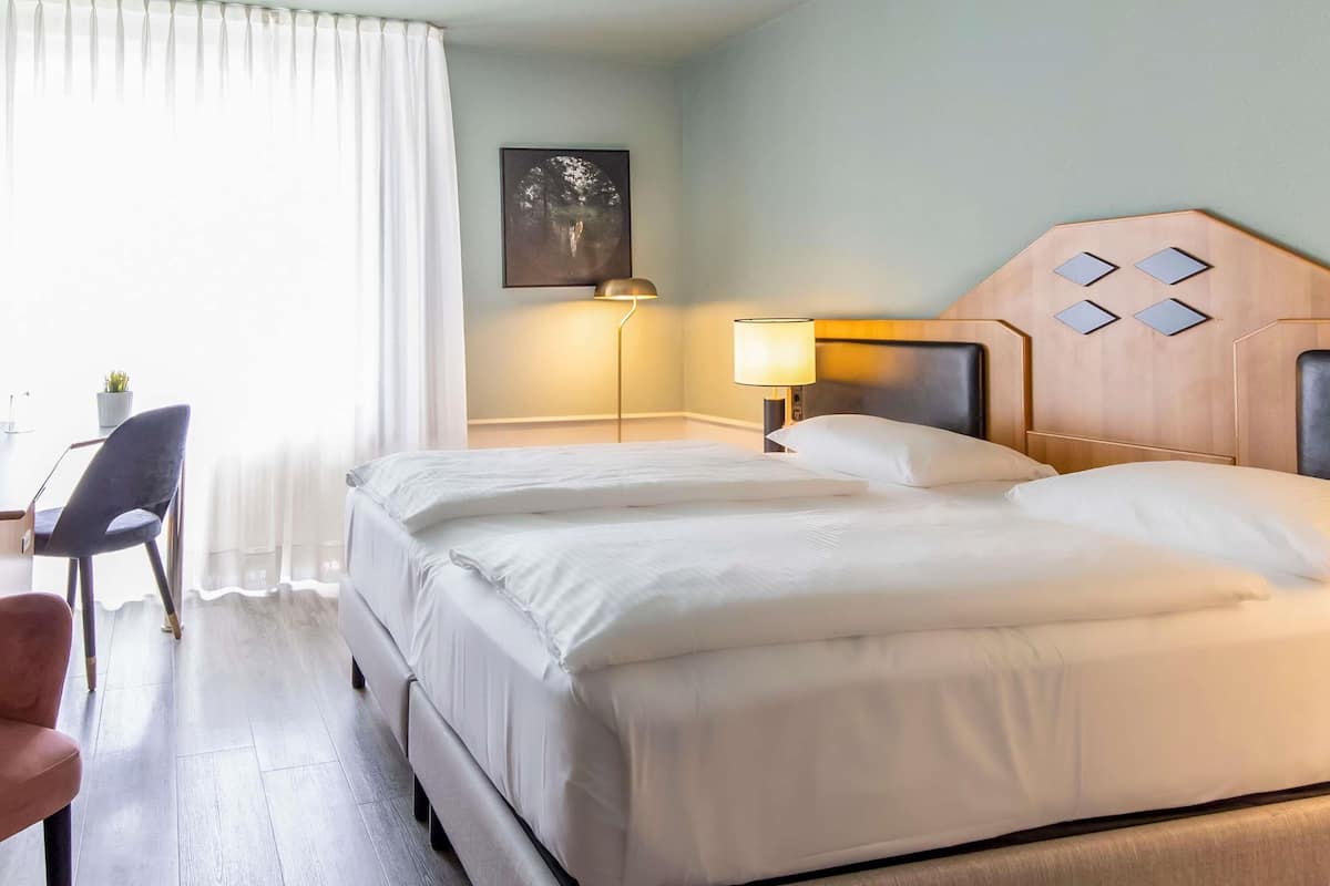 Habitación de hotel con una cama doble, un escritorio con silla, una lámpara y un cuadro en la pared.