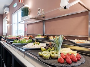 Buffet com diversos alimentos, incluindo frutas, queijos e saladas.