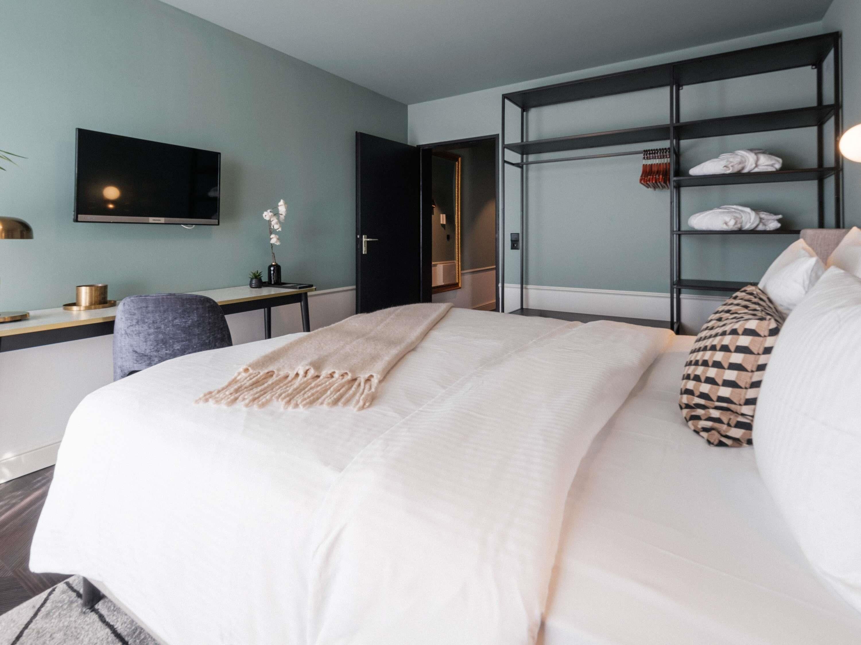 Una habitació d'hotel moderna amb un llit gran, un escriptori, una cadira i una televisió penjada a la paret.