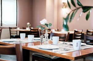 A dining area with wooden tables, white plates, cups, and a decorative glass bottle with a white rose.