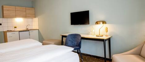 A hotel room with a bed, a desk, a chair, a TV, and a kitchenette.