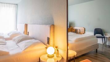 A hotel room with two beds, a round table with a lamp, a chair, and a large mirror.