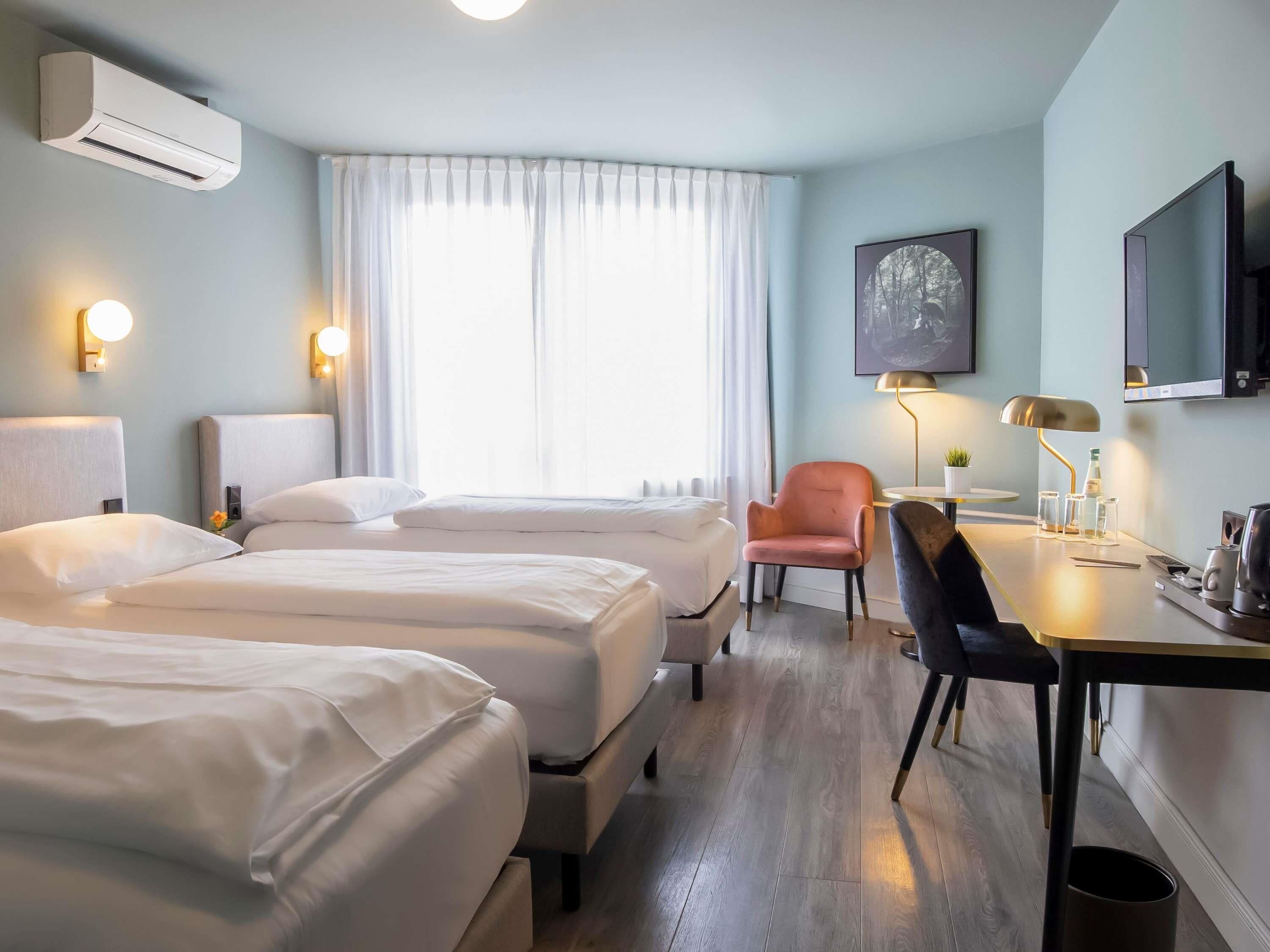 A hotel room with two beds, a desk with a lamp, a chair, a TV, and a painting on the wall.