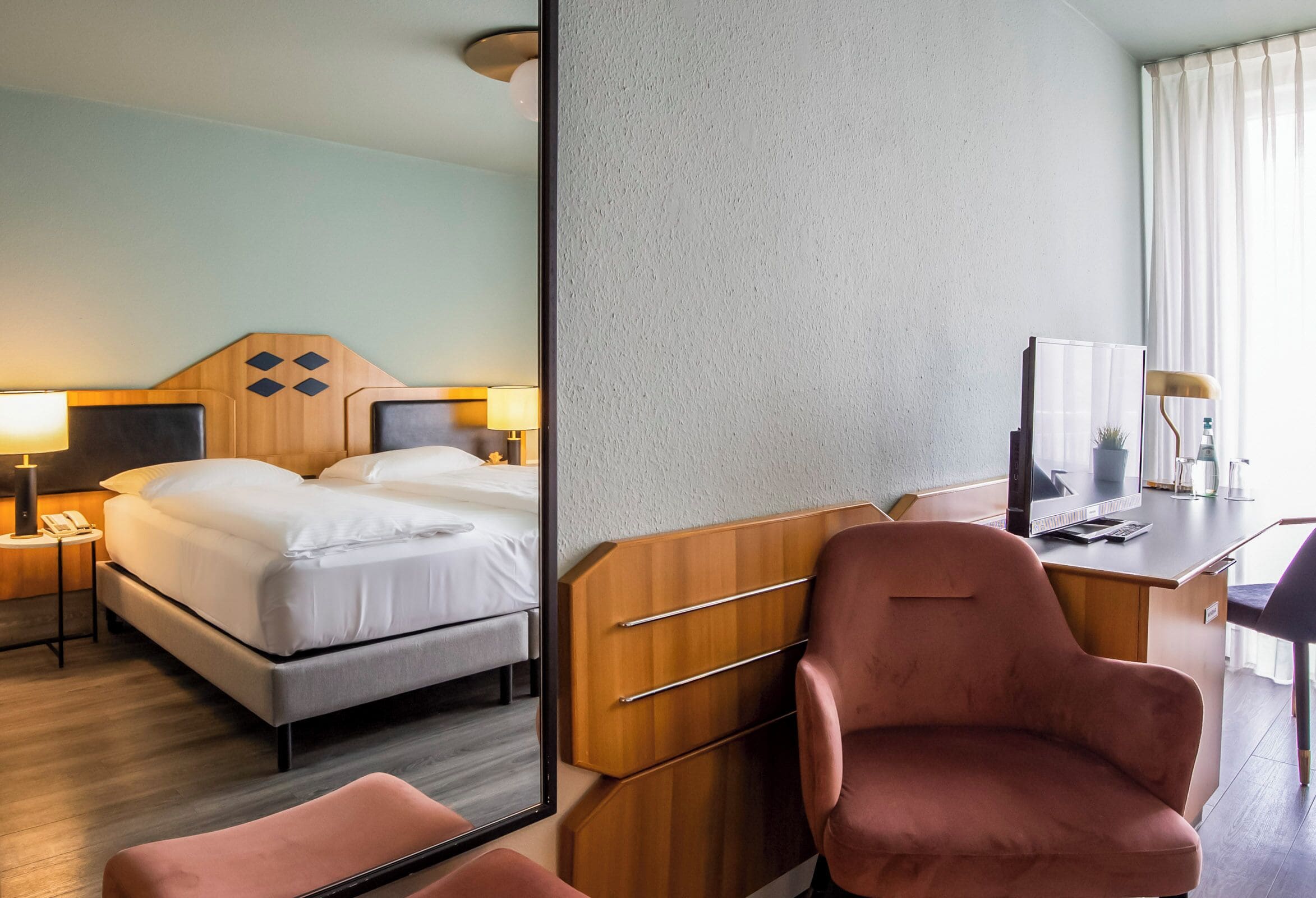 A hotel room with a bed, bedside tables, a desk with a chair, and a mirror.