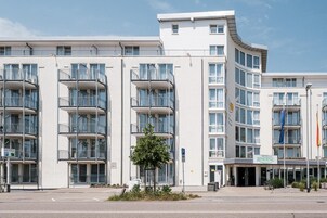 A modern hotel building with multiple balconies, a central entrance, and a visible parking sign.