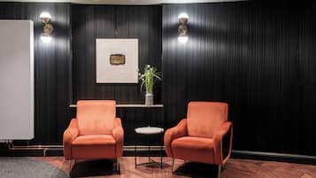 Une pièce avec deux fauteuils orange, une petite table ronde, une plante en pot et un tableau encadré accroché au mur.