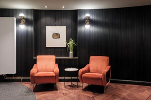 A room with two orange armchairs, a small round table, a potted plant, and a framed picture on the wall.