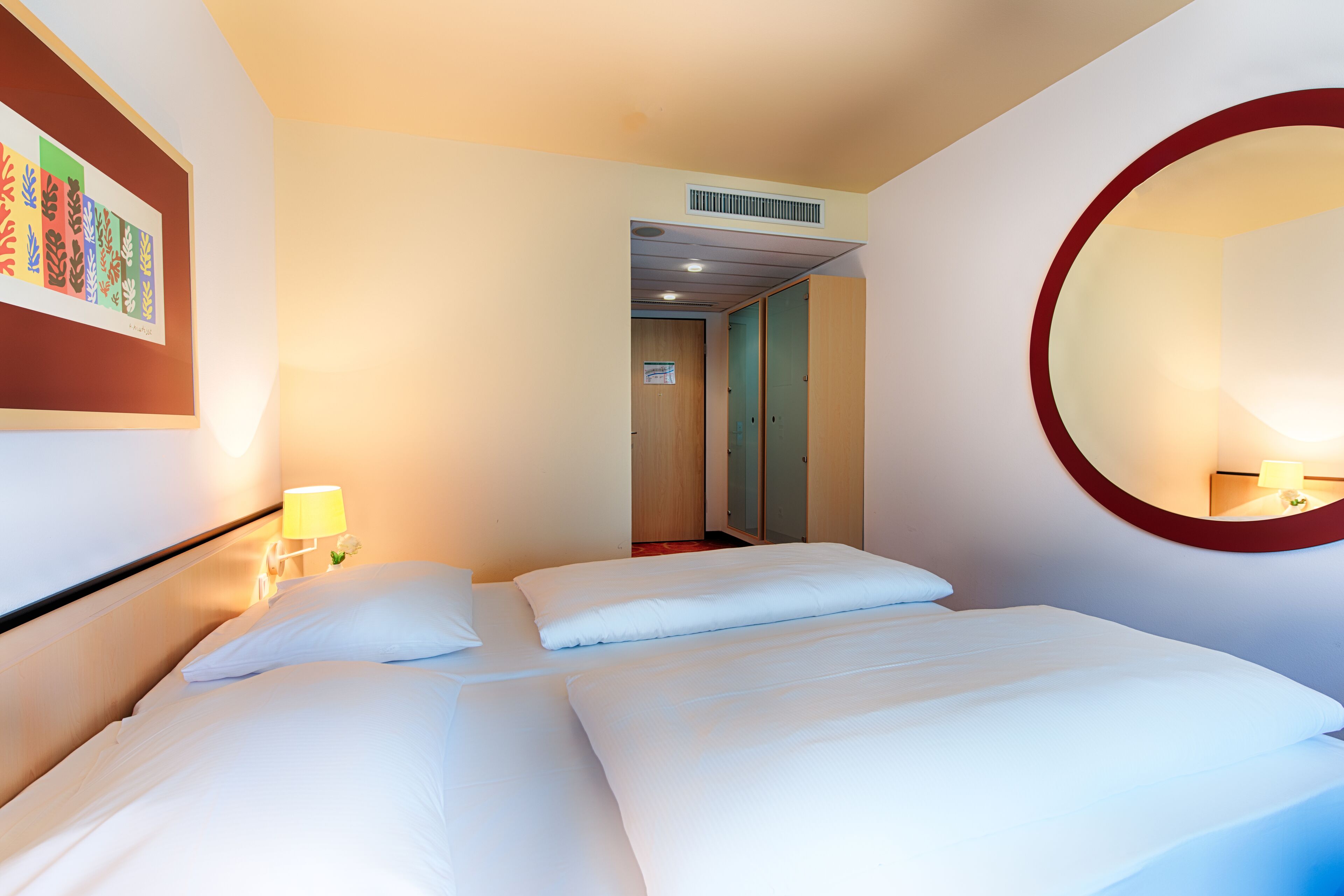 Habitación de hotel con dos camas, un espejo en la pared y una obra de arte enmarco.