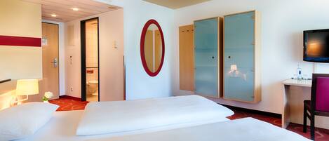 Habitación de hotel con dos camas, televisión, escritorio y espejo.