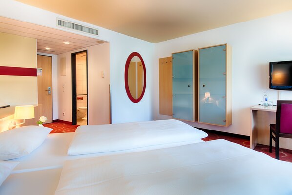 A hotel room with two beds, a TV, a desk, and a mirror. - Welcome Kongresshotel Bamberg (Bamberg)