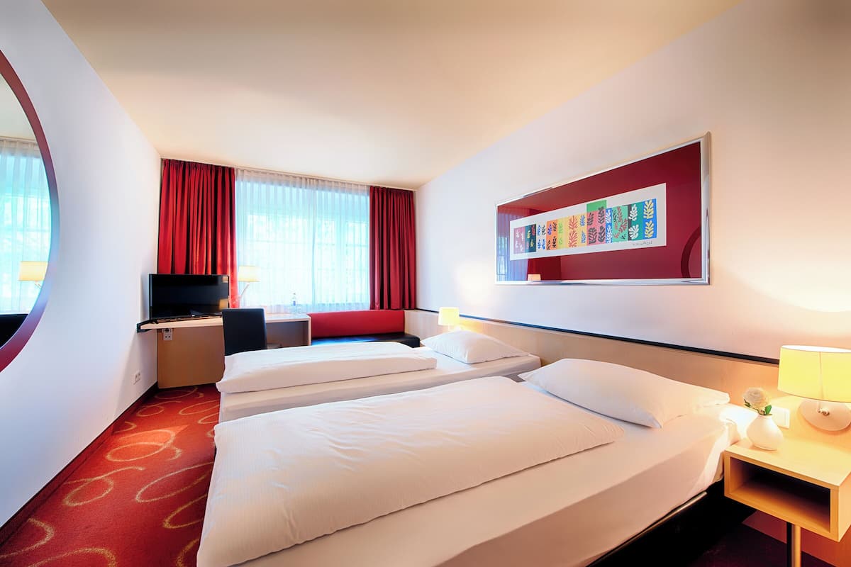 A hotel room with two beds, a desk, a television, and a window with curtains.