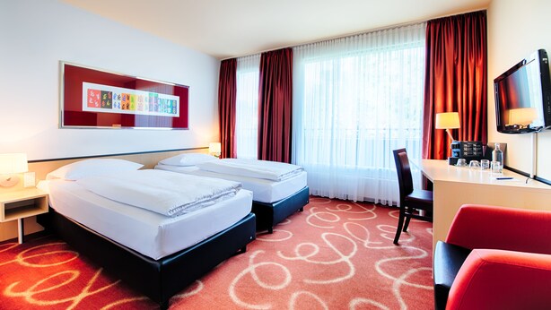 Une chambre d’hôtel avec deux lits, un bureau, une chaise, une télévision et une fenêtre avec des rideaux.