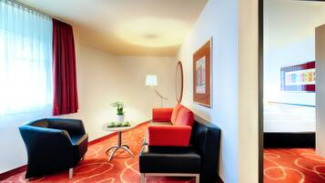 A hotel room with a red carpet, a black leather armchair, a red sofa, a small table with a plant, and a lamp.