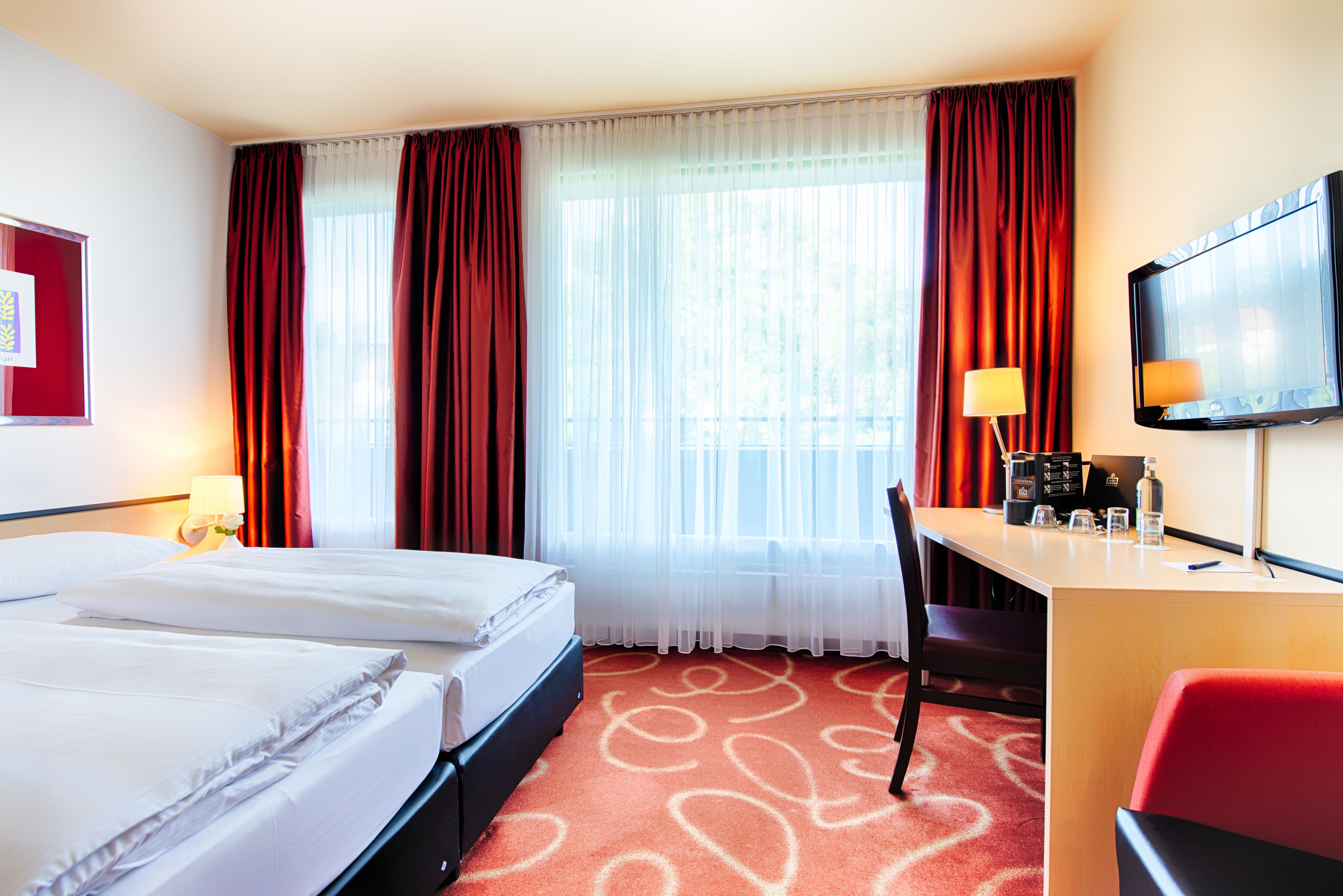 A hotel room with two beds, a desk with a chair, a TV, and a window with curtains.