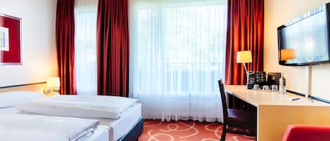 A hotel room with two beds, a desk with a chair, a TV, and a window with curtains.
