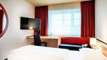 A hotel room with a bed, a desk, a chair, a TV, a lamp, and a window with curtains.