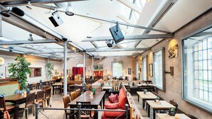 Un restaurant spacieux avec de hauts plafonds, des poutres apparentes et de grandes fenêtres. Les tables et les banquettes sont disposées de manière à faciliter la restauration.