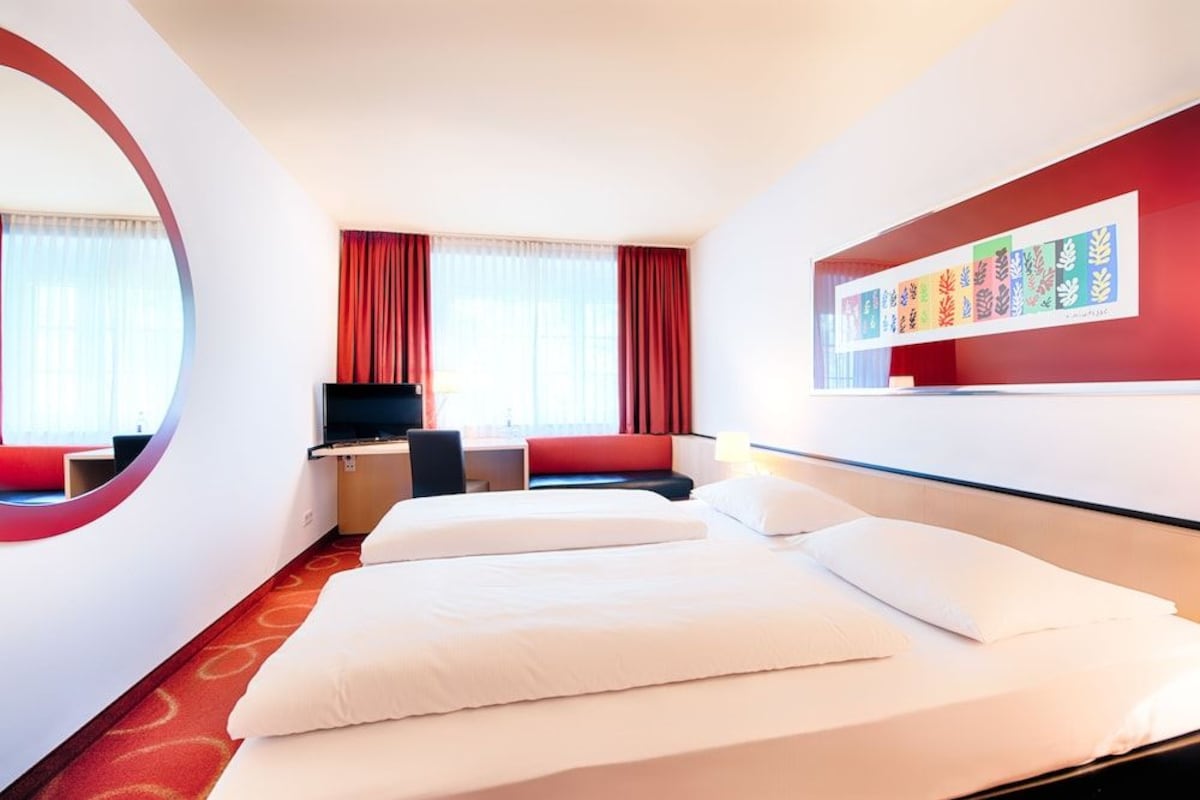 Habitación de hotel con cama, escritorio, silla, televisor y un cuadro llamativo en la pared.