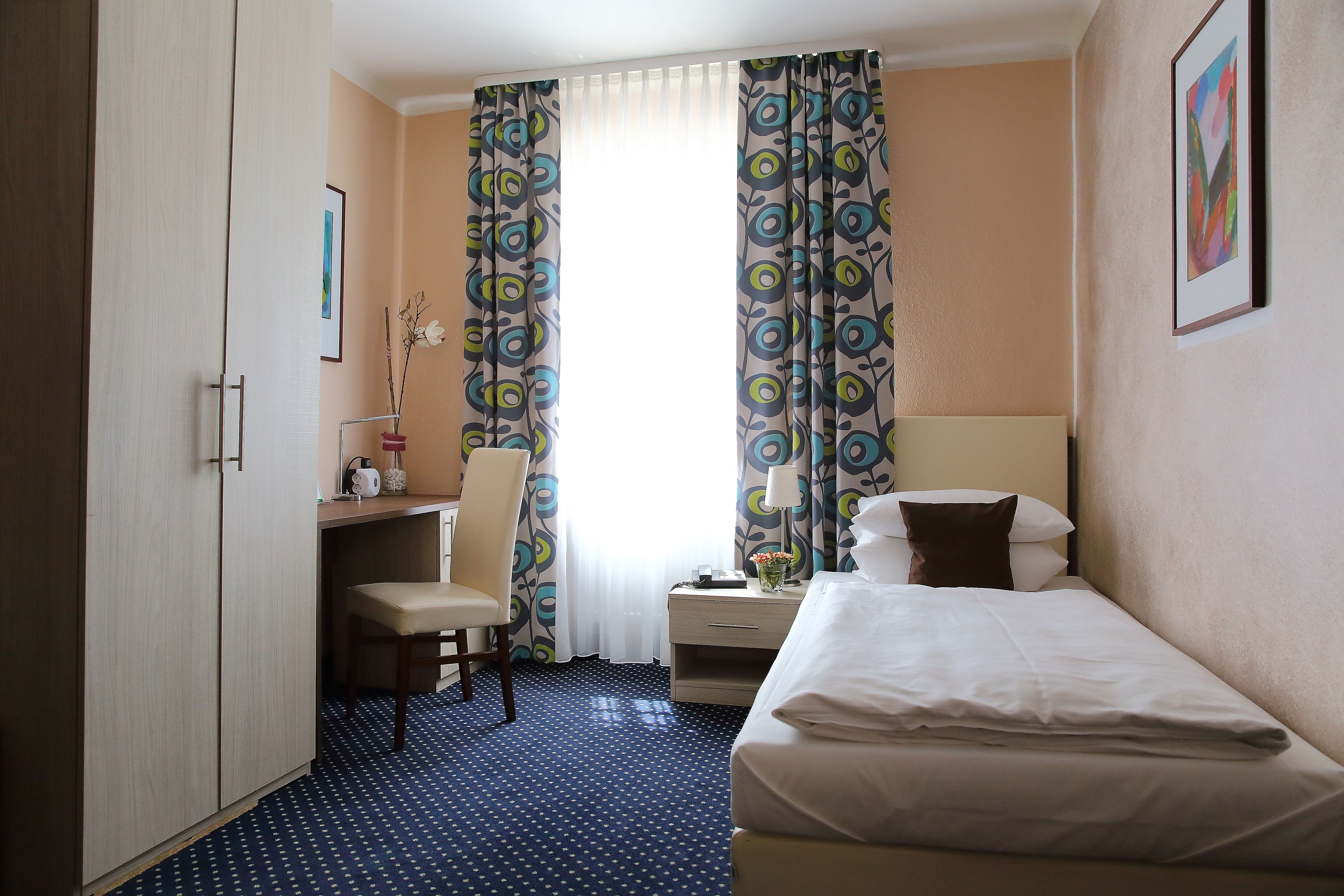 A hotel room with a bed, a desk, a chair, and a window with curtains.