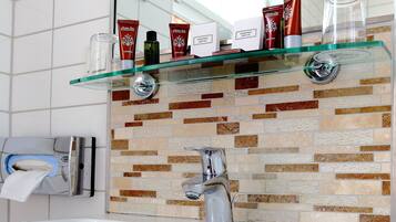 A bathroom with a white sink, a glass shelf with toiletries, a mirror, and a tiled backsplash.