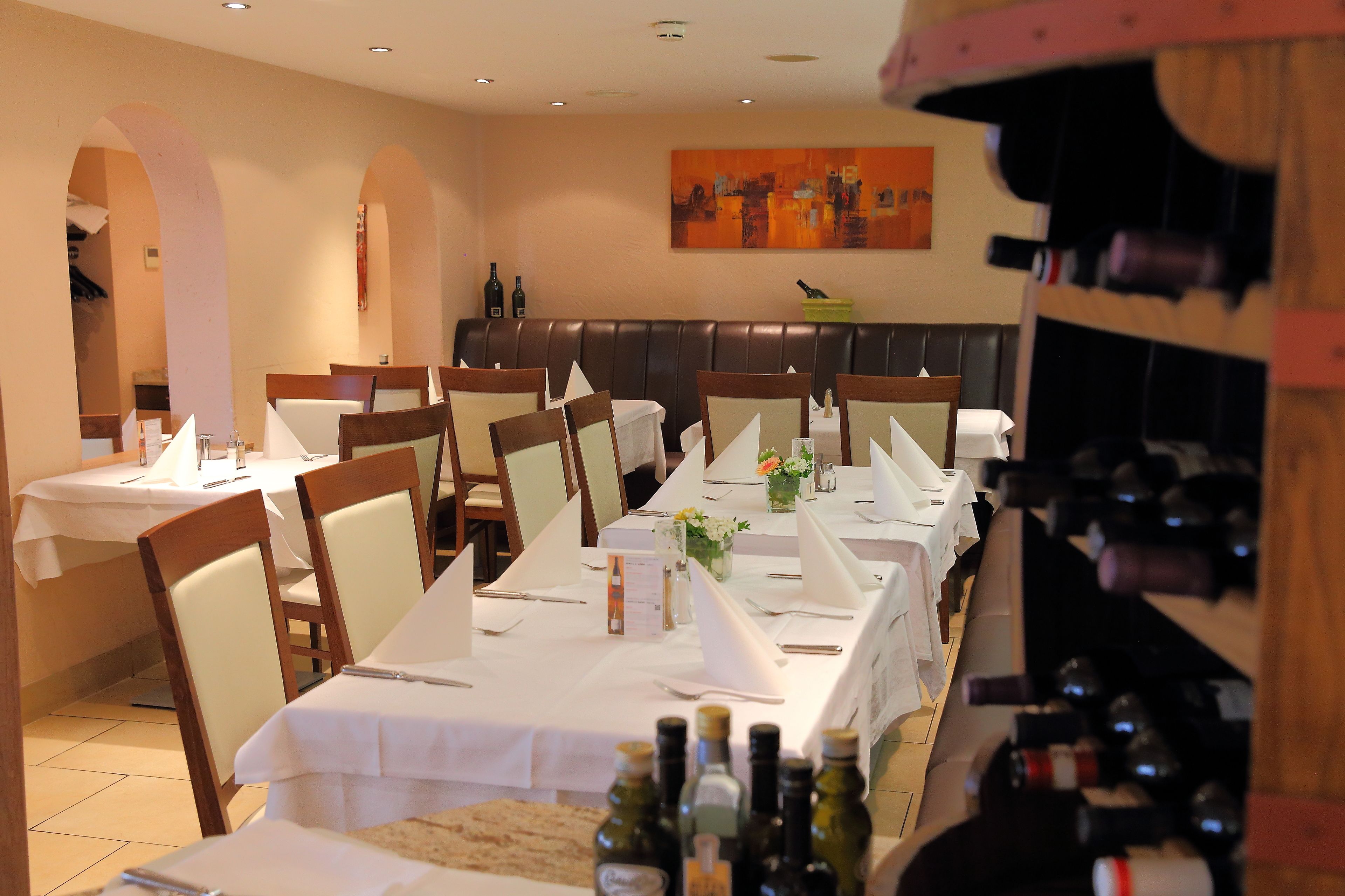 A dining area with tables set for service, a wine rack, and a painting on the wall.
