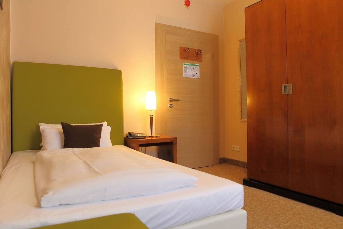 A hotel room with a bed, bedside table, lamp, and a wardrobe.