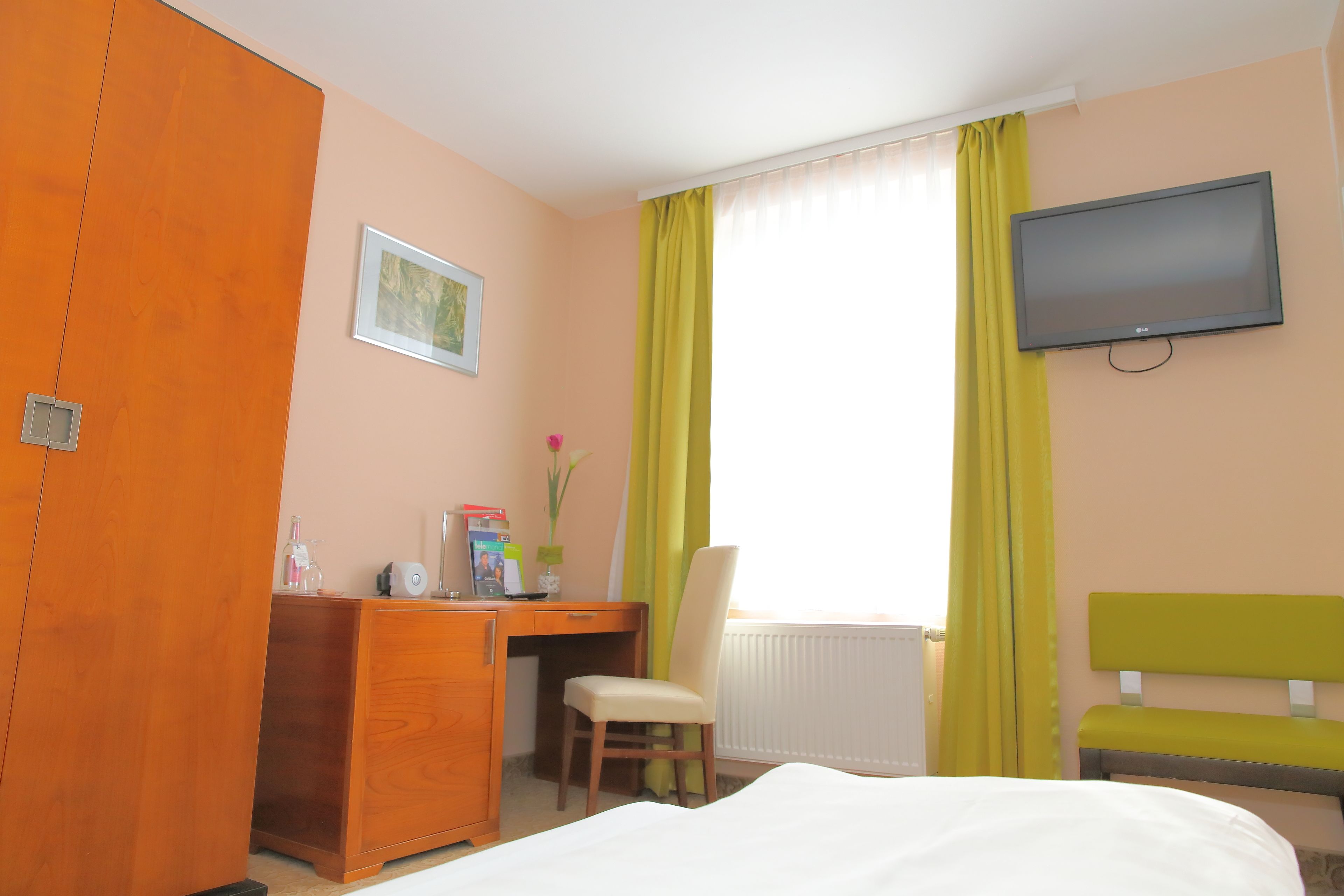 Een hotelkamer met een bed, een bureau, een stoel, een televisietoestel en een raam met gordijnen.