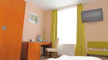 Een hotelkamer met een bed, een bureau, een stoel, een televisietoestel en een raam met gordijnen.