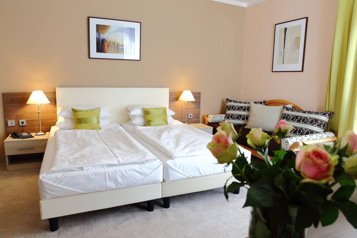 A hotel room with a double bed, two bedside tables, two lamps, a nightstand, a chair, and a vase with flowers.