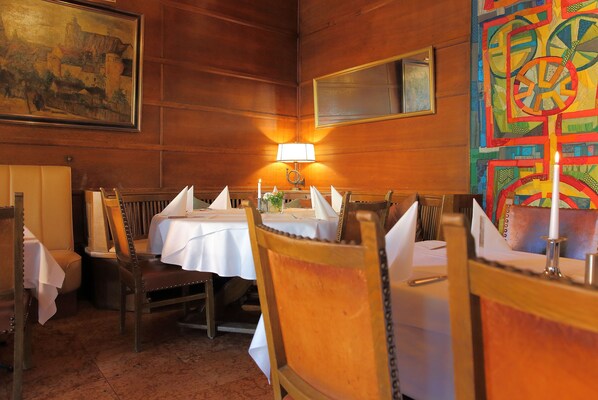 A dining area with wooden walls, a table set with white tablecloths, chairs, and a candle.