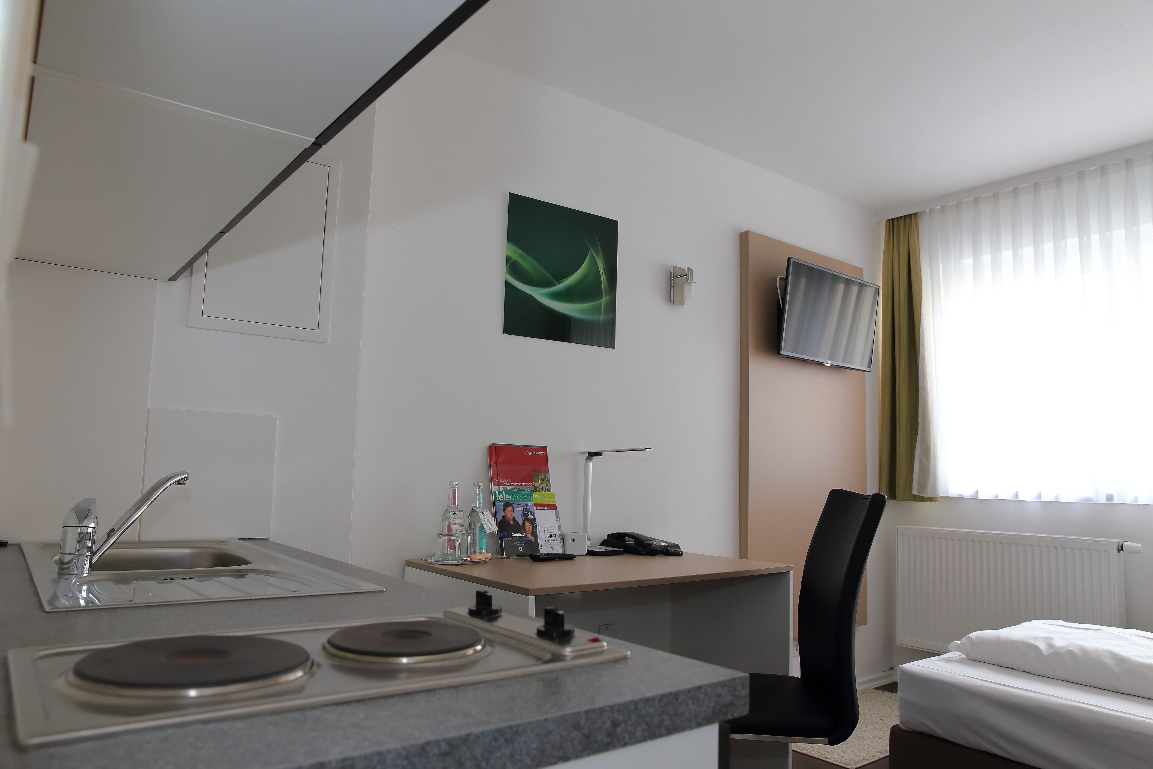 A hotel room with a kitchenette, a bed, a TV, and a window with curtains.