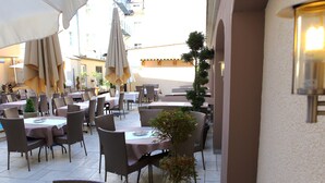 Un área de café al aire libre con mesas, sillas, sombrillas y plantas en macetas.