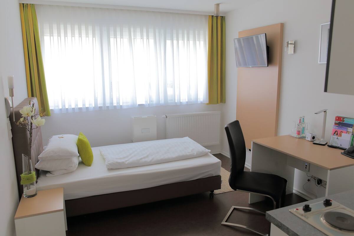 A hotel room with a bed, a desk, a chair, a TV, and a radiator.