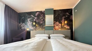 Habitación de hotel con cama doble, mesita de noche, lámpara y un amplio mural abstracto en la pared.