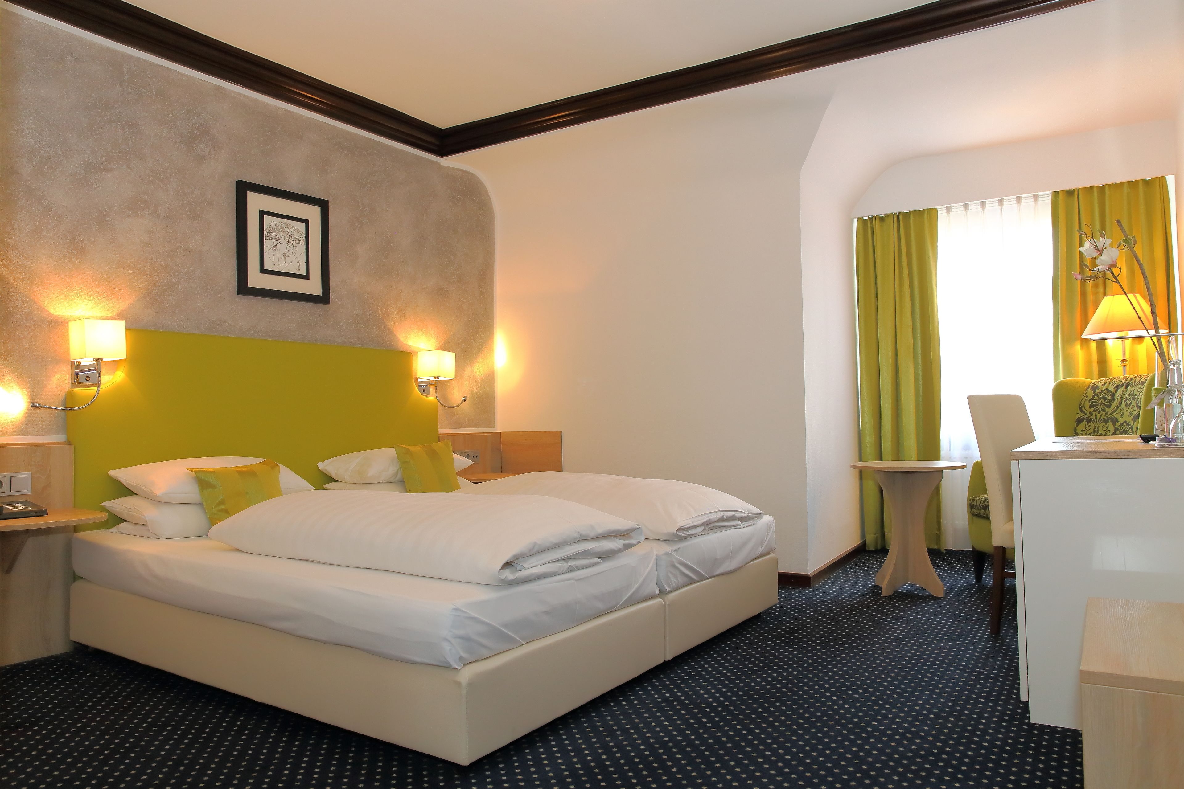 Una camera d'albergo con un letto, abat-jour, una scrivania e una sedia.