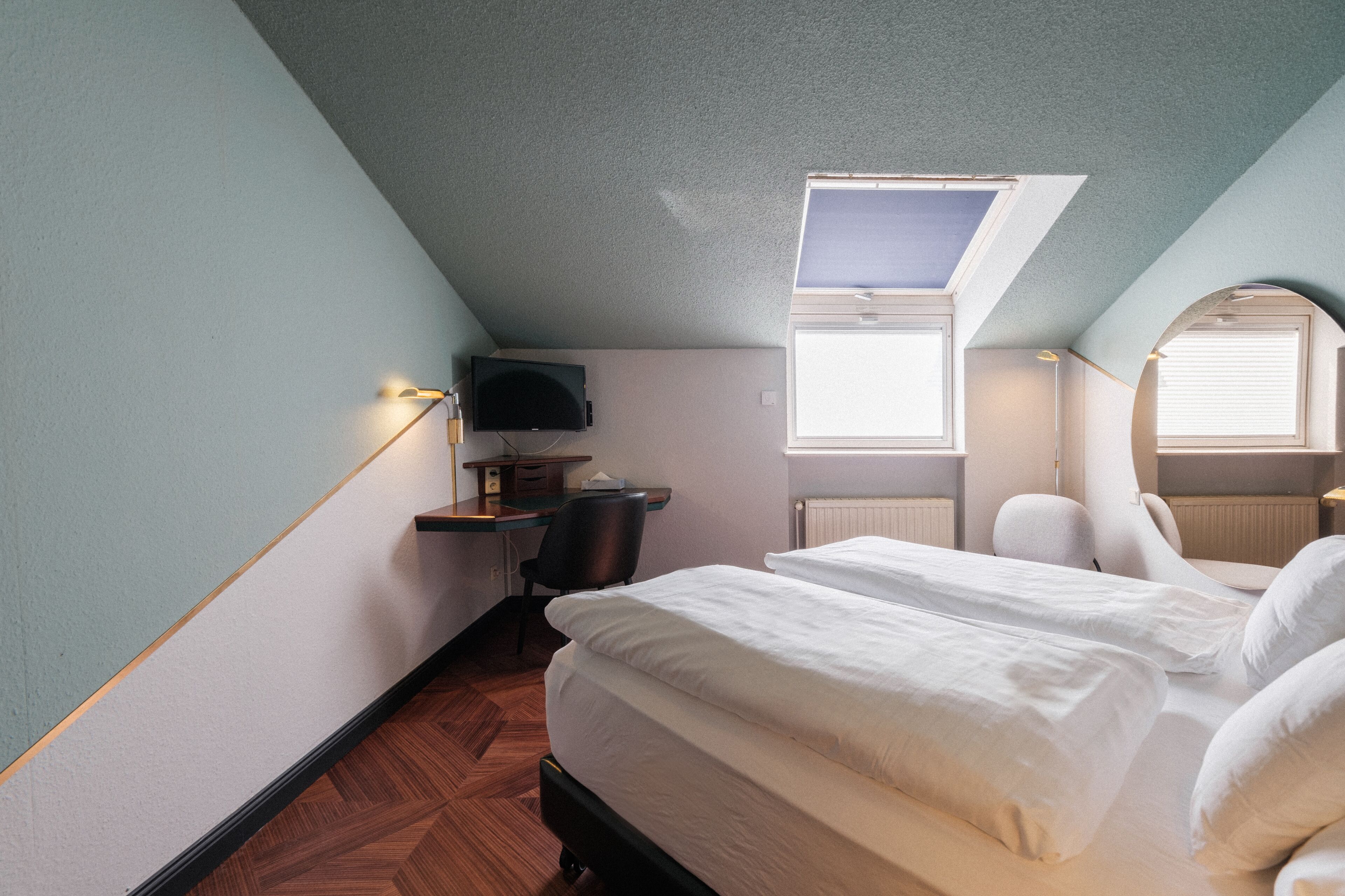 A bedroom with a bed, a desk, a chair, a television, and a skylight.