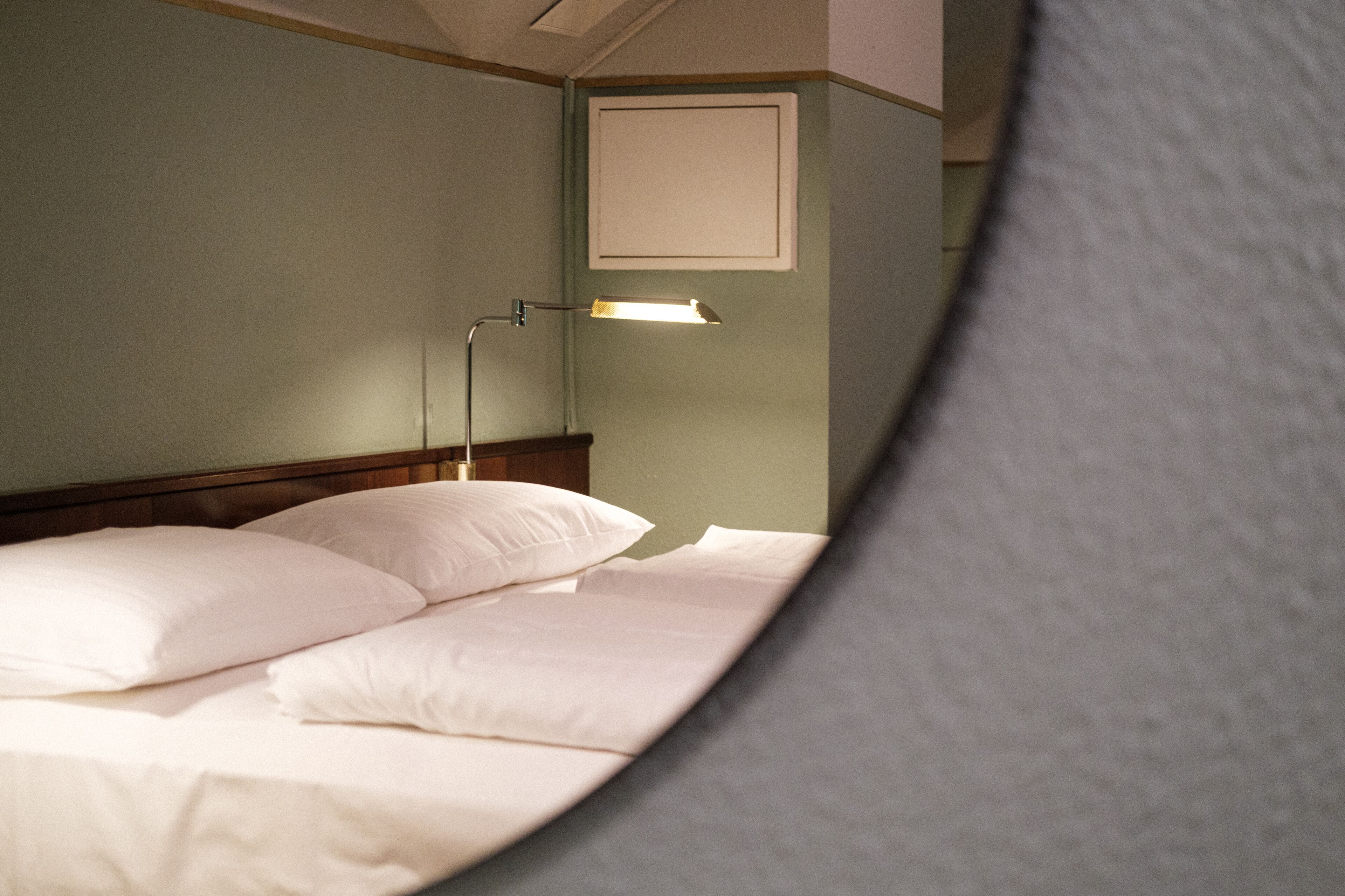 Een bed met witte lakens, een nachtkastje en een wandlamp.
