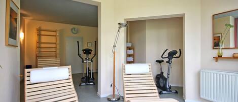 Una habitación con dos sillones de madera, una lámpara de pie, bicicletas estáticas, una escalera, un reloj y un radiador.
