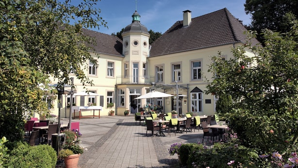 A courtyard with outdoor seating, a building with a tower, and potted plants. - Hotel Haus Duden (Wesel)