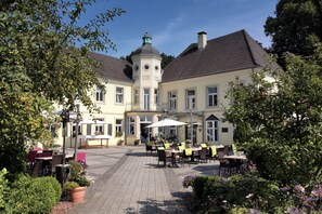 A courtyard with outdoor seating, a building with a tower, and potted plants. - Hotel Haus Duden (Wesel)