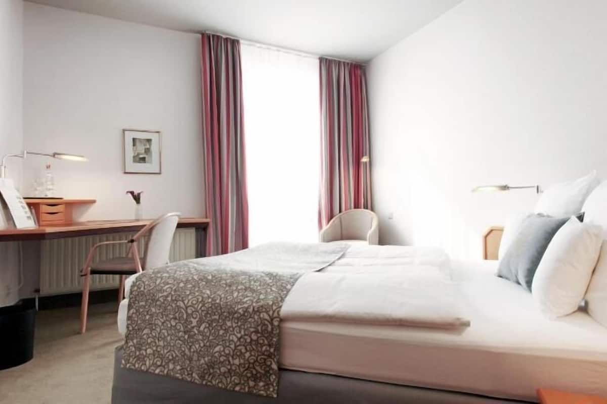 Ein Hotelzimmer mit Bett, Schreibtisch, Stuhl und einem fensterbepflanzten Fenster.