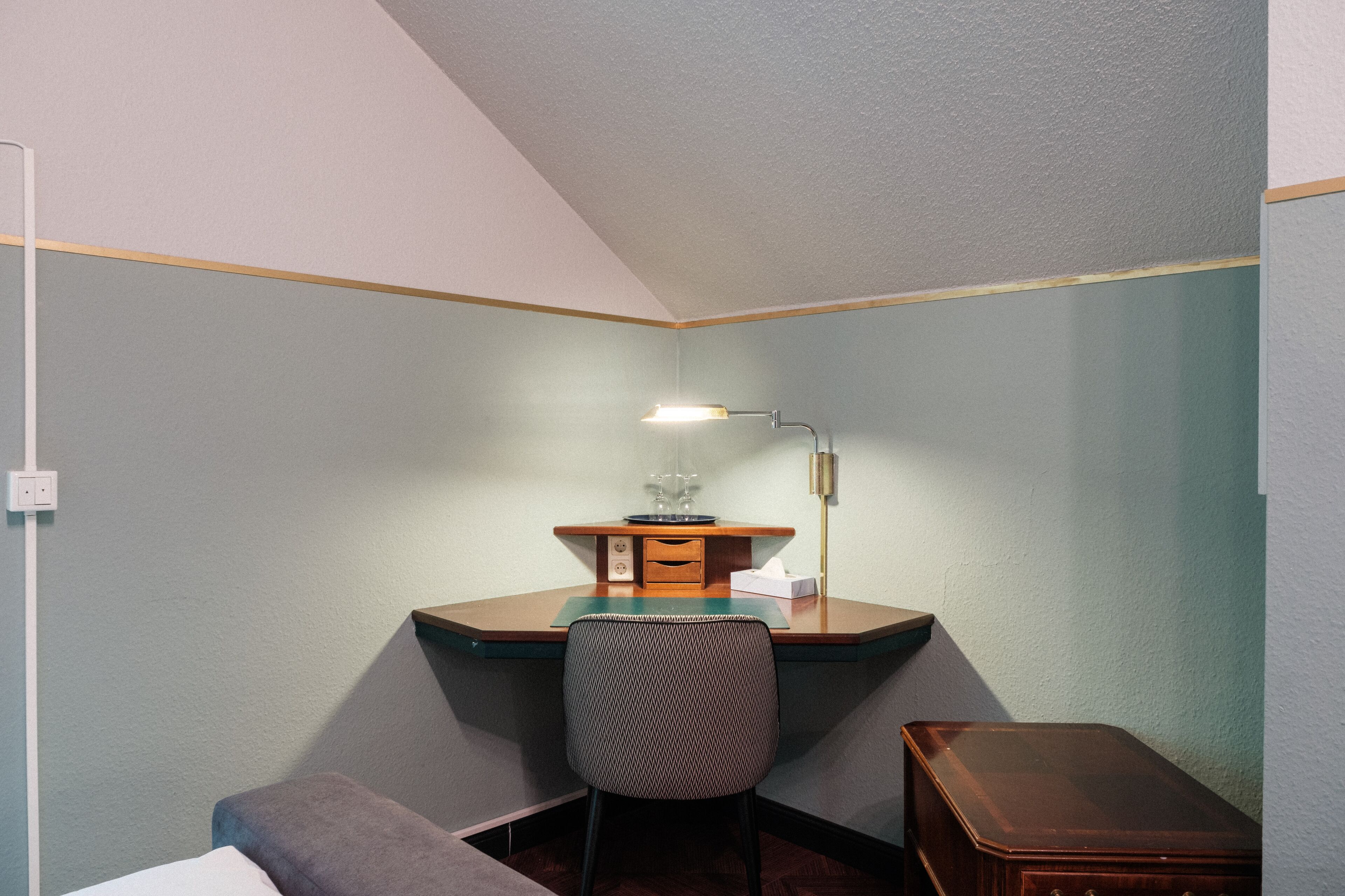 Habitación de esquina con escritorio, silla y un pequeño armario de madera.