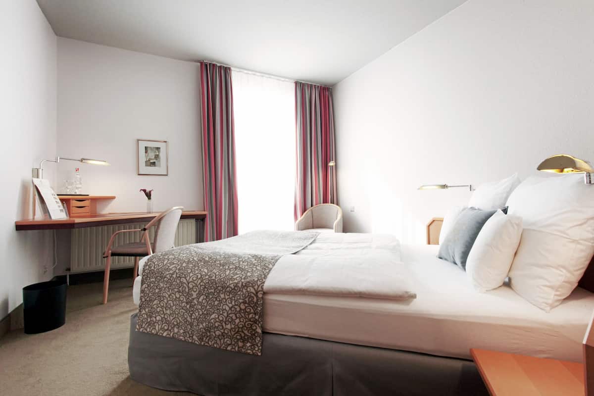 Ein Hotelzimmer mit Bett, Schreibtisch, Stuhl und Heizkörper.