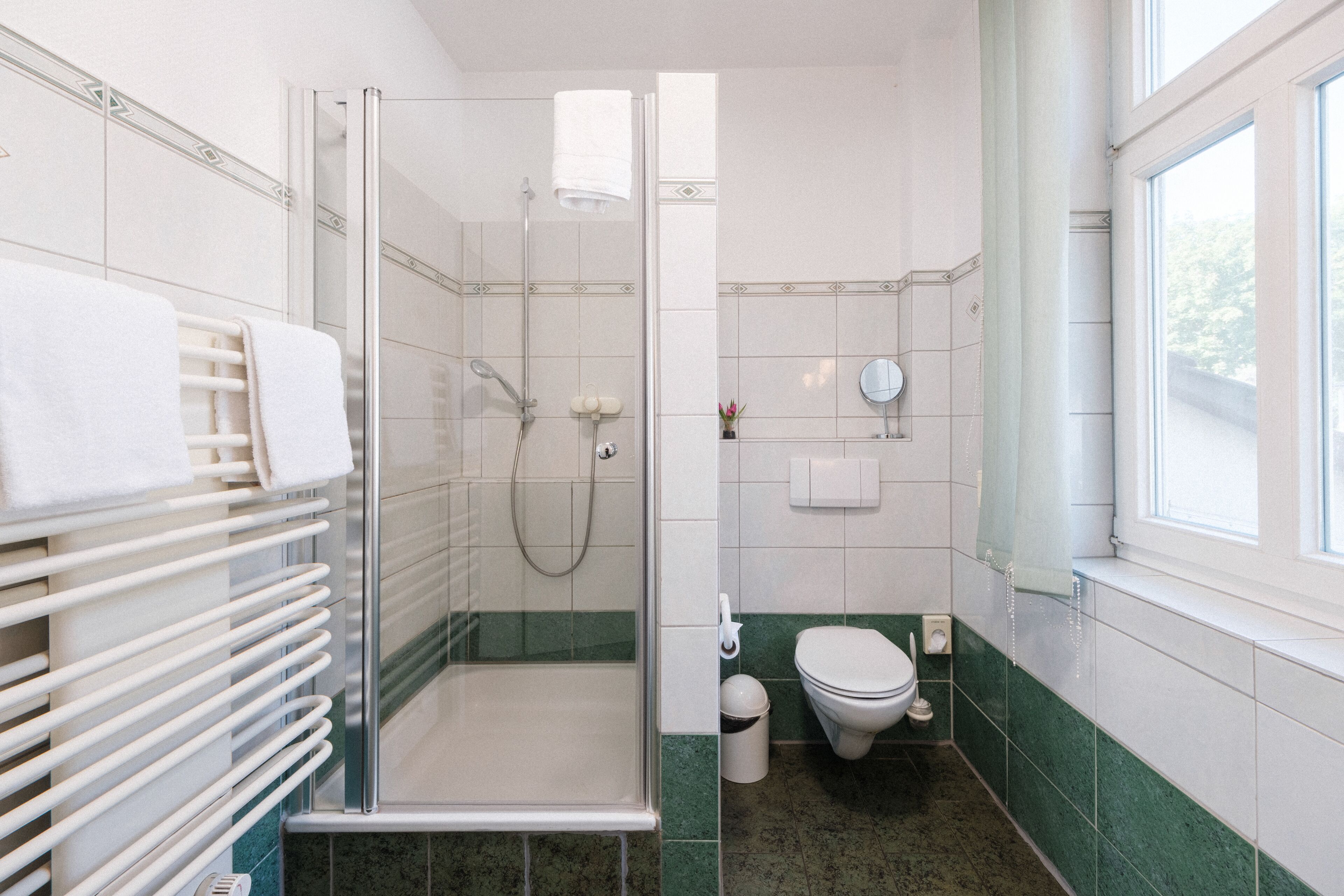 A bathroom with a glass-enclosed shower, a toilet, and a towel rack with towels.